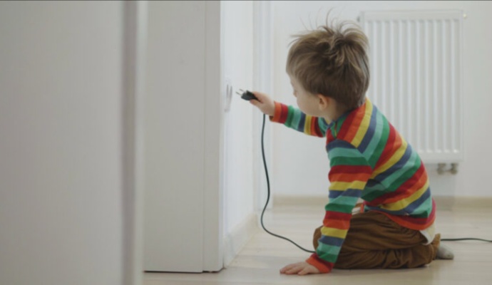 Children reaching toward an electrical wall outlet with a power plug
