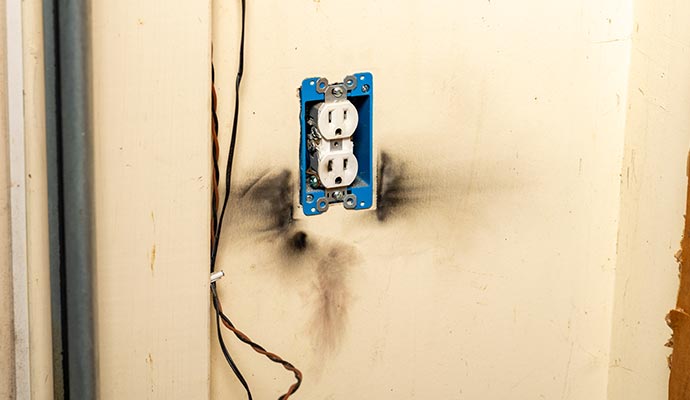 Burnt electrical outlet box inside a wall showing severe fire damage.