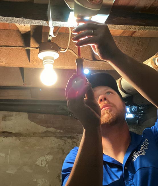 Electrician performing an indoor lighting repair in a basement.