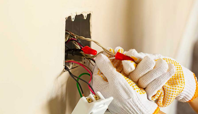 An expert repairing electrical wiring inside a wall outlet box