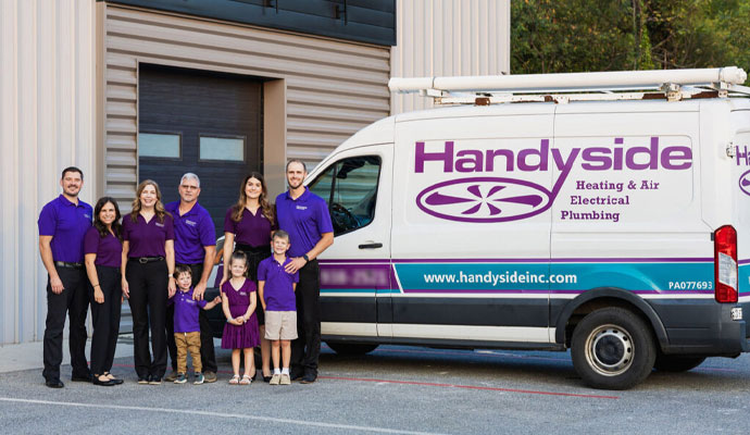 Handyside Plumbing, HVAC & Electrical owners with family wearing purple Handyside branded shirts standing in front of a white company service van and a warehouse building
