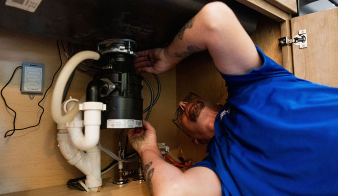 Plumber repairing pipes and garbage disposal under a sink.