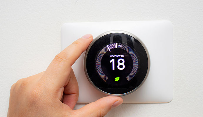 Person adjusting a smart digital thermostat on a wall.