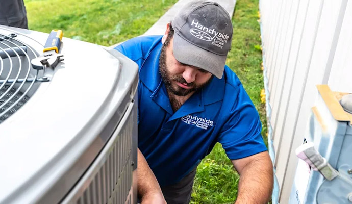 A Handyside technician checking and refilling refrigerant levels in an outdoor AC unit
