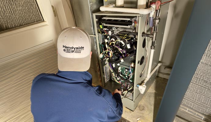 Technician repairing HVAC furnace system wiring.