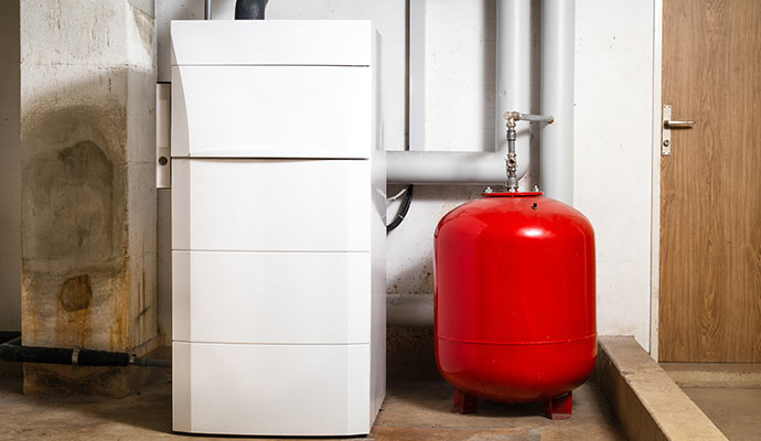 Modern white boiler heating unit with red expansion tank in utility area