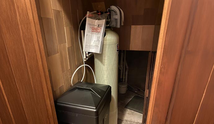 Home water softener installed in a wood paneled wall.