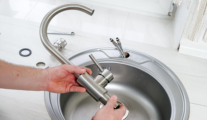 Plumber installing modern steel kitchen faucet.