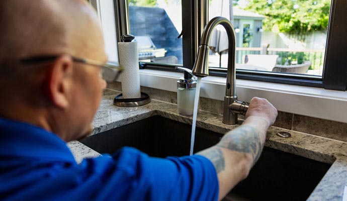 Professional plumber testing modern kitchen faucet water flow.