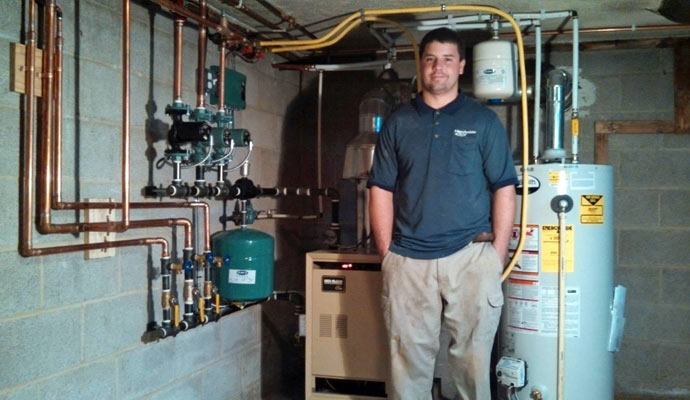 Technician of Handyside Plumbing, HVAC & Electrical standing beside a boiler system in a basement