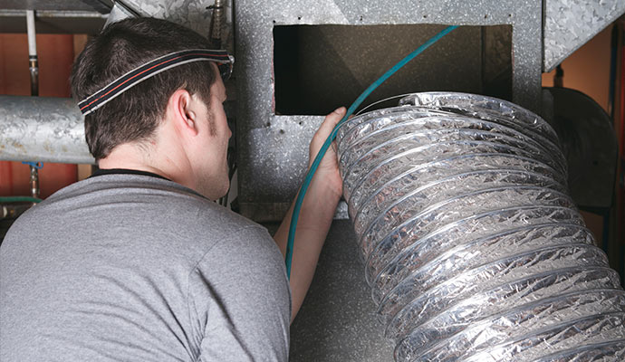 HVAC technician with headlamp performing air duct cleaning with flexible vacuum hose